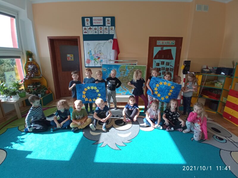 Na zdjęciu dzieci prezentują wykonane dwie duże flagi Unii Europejskiej.