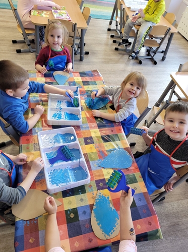 Dzieci malują kartonowe krople wałkiem maczanymw farbie.