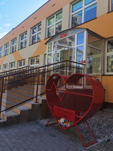 Czerwony pojemnik na nakrętki umiejscowiony przy wejściu do budynku przedszkola