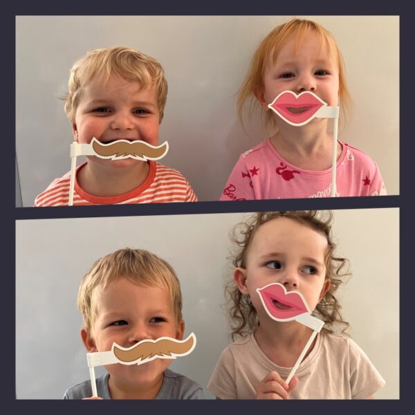 Dzieci na zdjęciu pozują z wąsami i ustami dużymi.