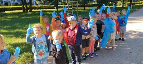  przedstawia grupę dzieci mającą na rękach założone gumowe, niebieskie rękawiczki. Dzieci znajdują się w parku.