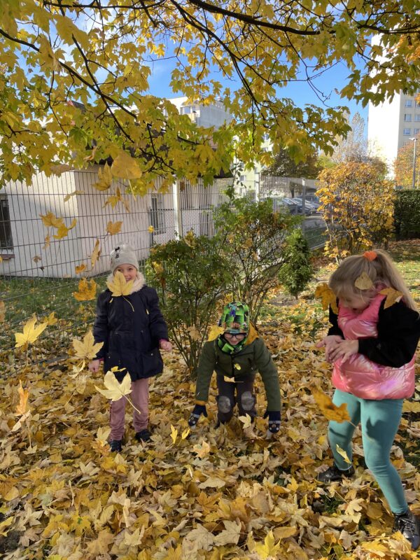 Dzieci podrzucają liśćmi do góry. Świetnie się przy tym bawią.