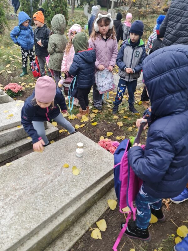 Dzieci sprzątają grób zmiatając z niego liście.
