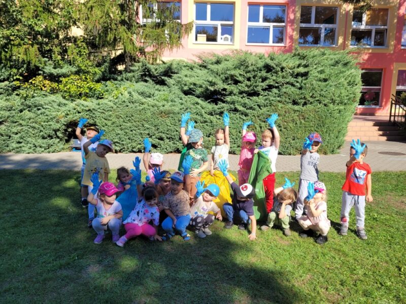 Zdjęcie grupowe dzieci na terenie ogrodu przedszkolnego. Dzieci mają założone niebieskie, jednorazowe rękawiczki.