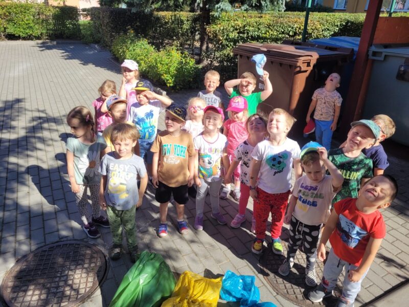 Zdjęcie przedstawia grupę dzieci z workami na śmieci do segregacji: niebieskim, zielonym i żółtym.