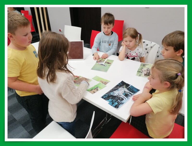 Sześcioosobowy zespół dzieci układa puzzle o zwierzętach przy stoliku.
