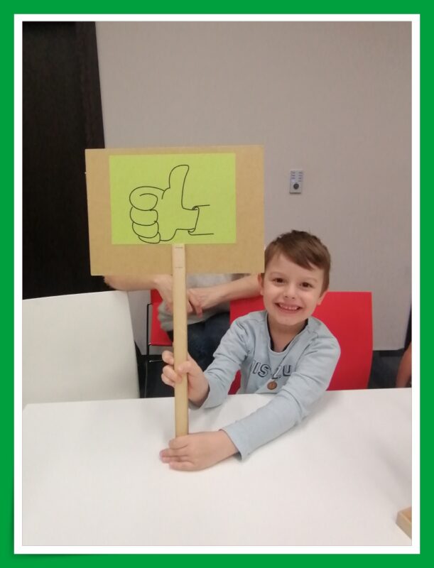 Jedno z dzieci prezentuje tabliczkę oceniającą z symbolem graficznym "OK".