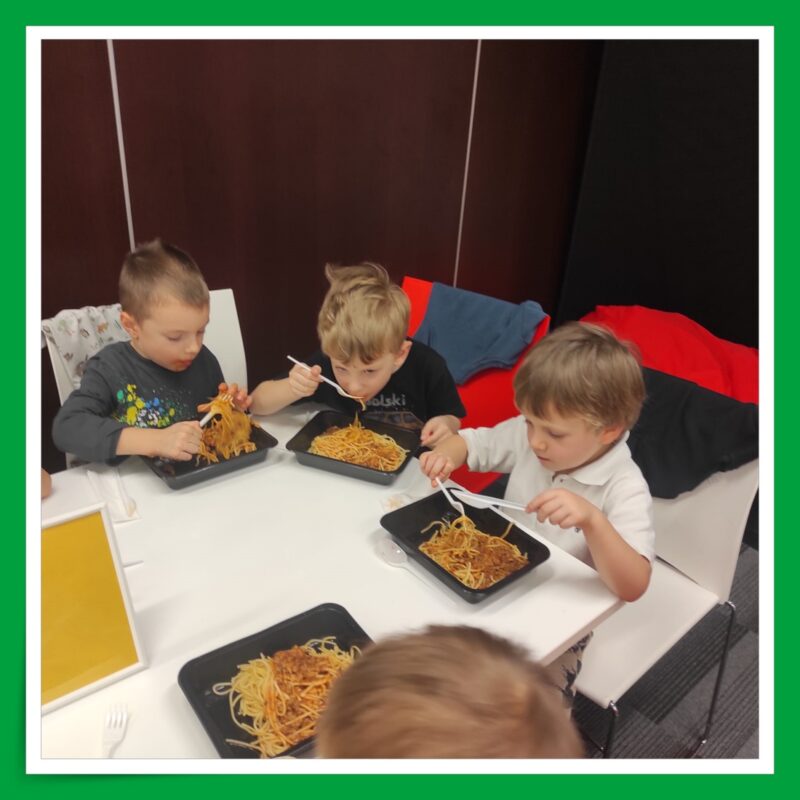 Troje dzieci z apetytem zajada spaghetti.