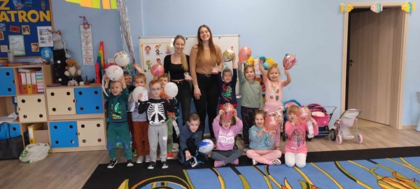 Zdjęcie pierwsze przedstawia grupę dzieci i dwie panie. Dzieci trzymają w dłoniach udekorowane według własnych pomysłów balony oraz naklejki.