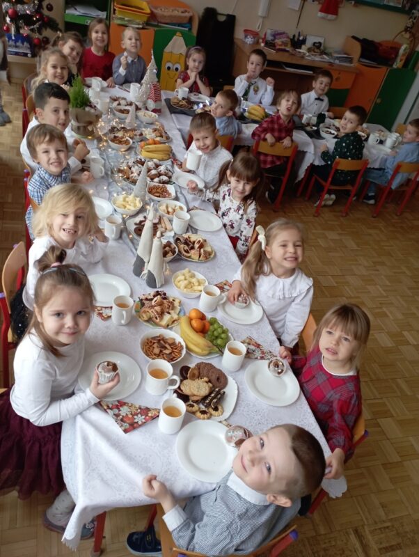 Na zdjęciu dzieci za świątecznie nakrytym stole, uśmiechają się do zdjęcia.