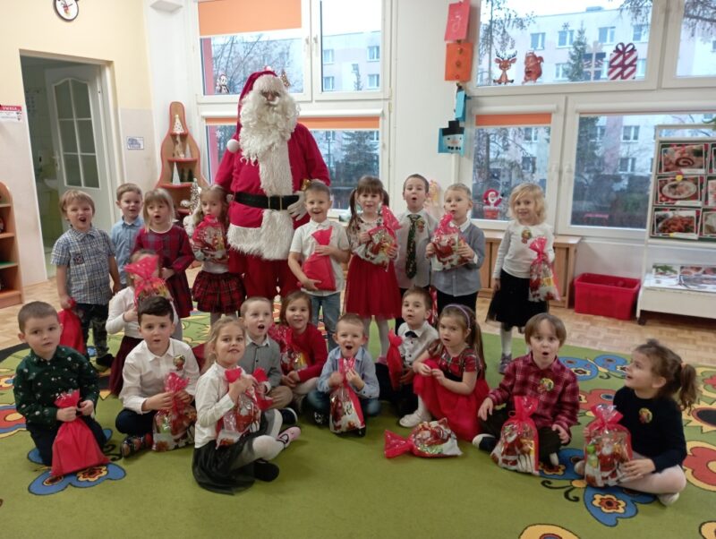 Zdjęcie grupowe ze Świętym Mikołajem - dzieci trzymają upominki od gościa.
