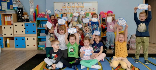  Zdjęcie czwarte przedstawia grupę dzieci trzymającą w dłoniach dyplomy. Dzieci stoją na tle tablicy z napisem " Dzień matematyki".