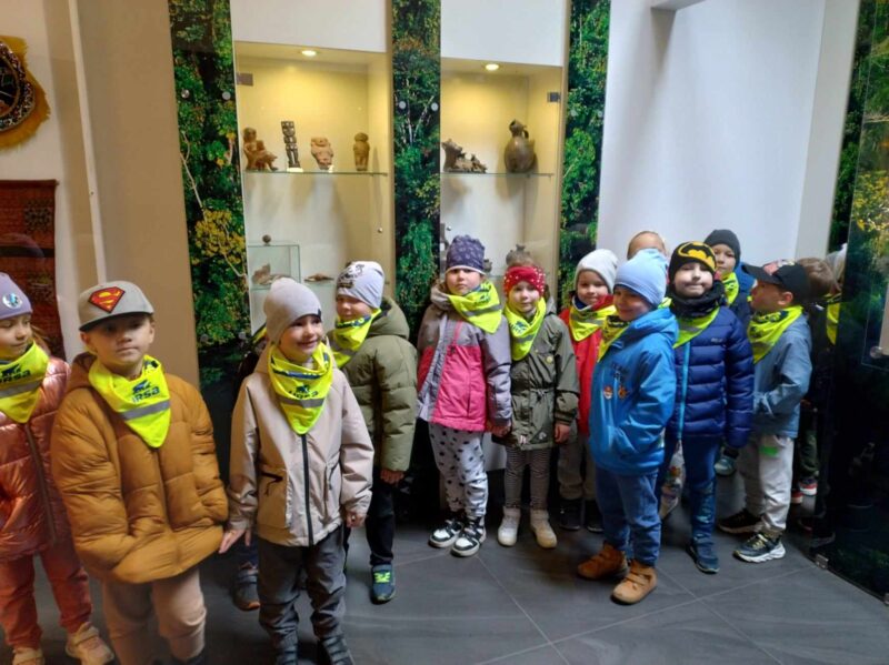 Zdjęcie drugie przedstawia grupę dzieci znajdującą się w muzeum. Dzieci stoją na tle eksponatów pochodzących z różnych stron świata.