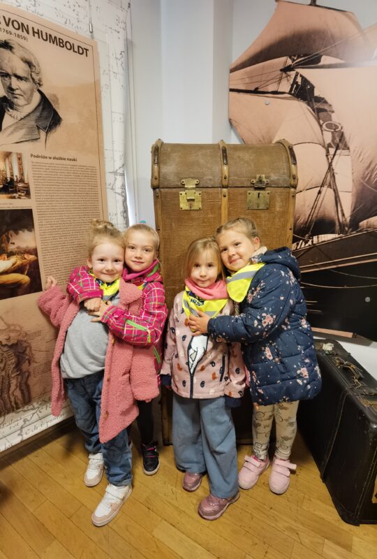 Cztery dziewczynki stoją  przed dużą walizką.