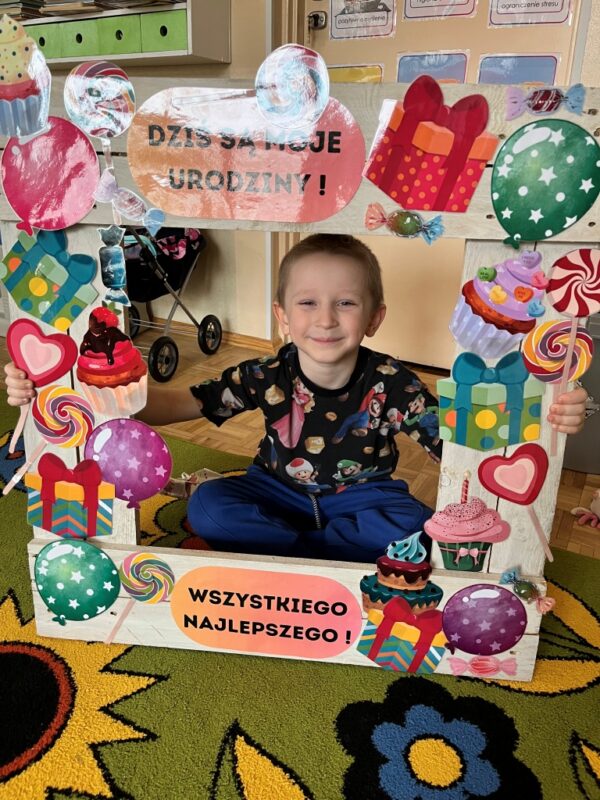 Chłopiec z radością i zadowoleniem pozuje do zdjęcia trzymając w dłoniach urodzinową fotobudkę. 