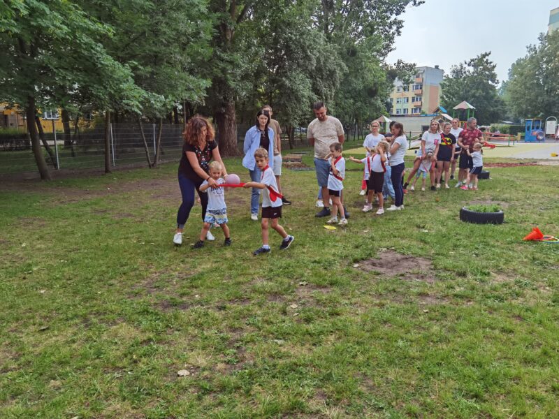 Rodzice i dzieci aktynwie uczestnicza w zabawach podczas przedszkolnej olimpiady.